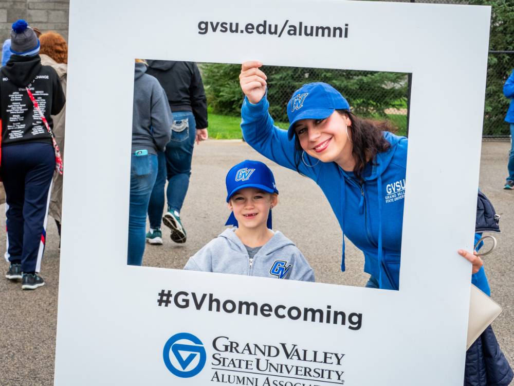Alumna and little Laker pose with #GVhomecoming sign